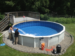 Above ground pool with a rock landscaping being filled with water by two men