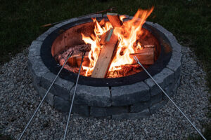 Retaining wall block fire pit with fire and roasting sticks